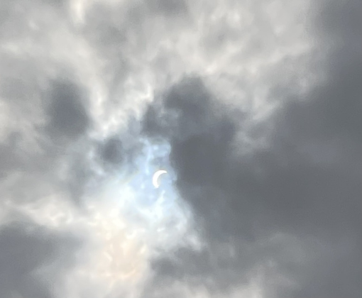 The partially eclipsed sun peaks through the clouds. 